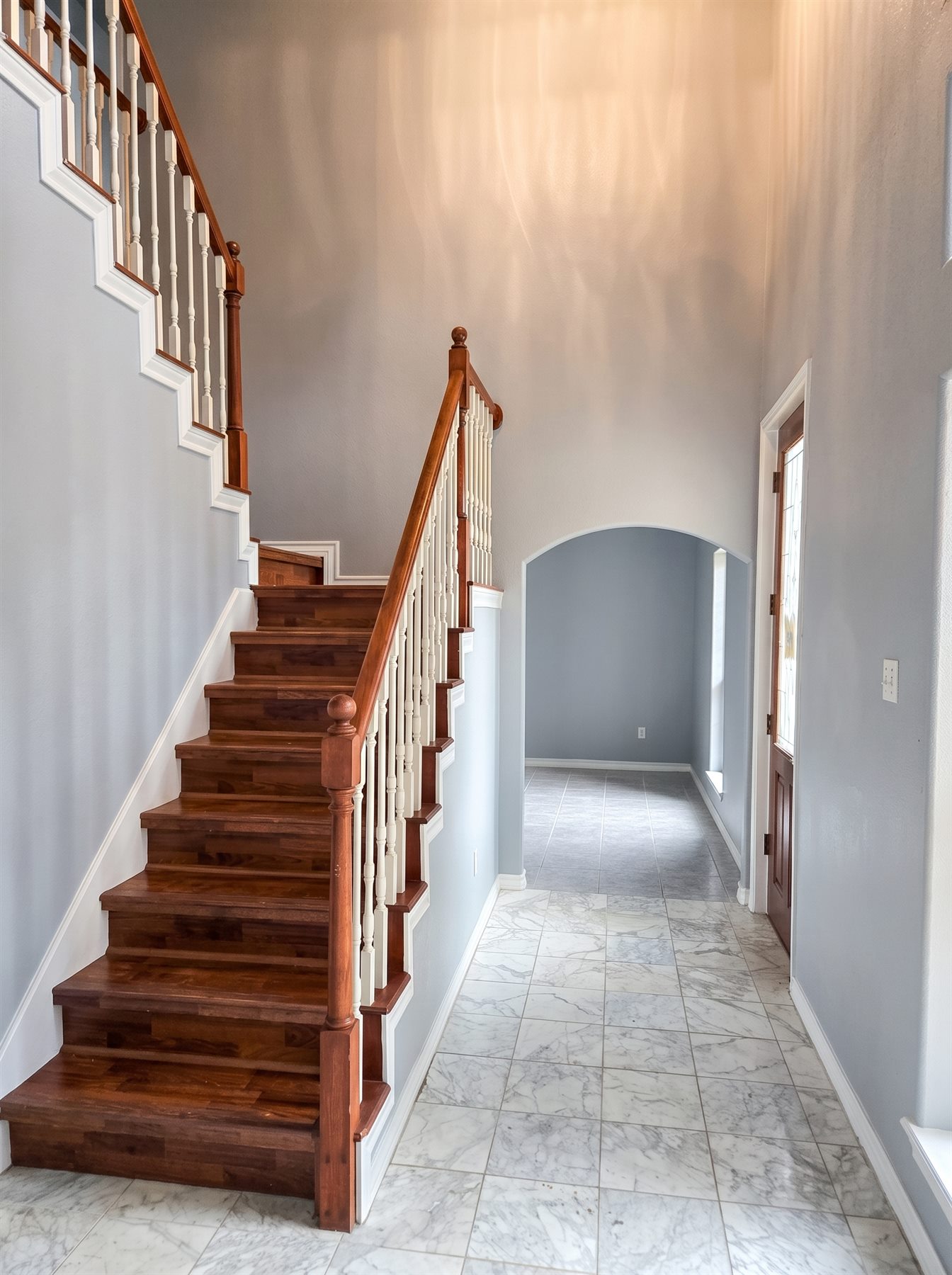 Finished two-story entryway with a rich wood staircase and marble tile floor by One Stop Solutions CC in Corpus Christi